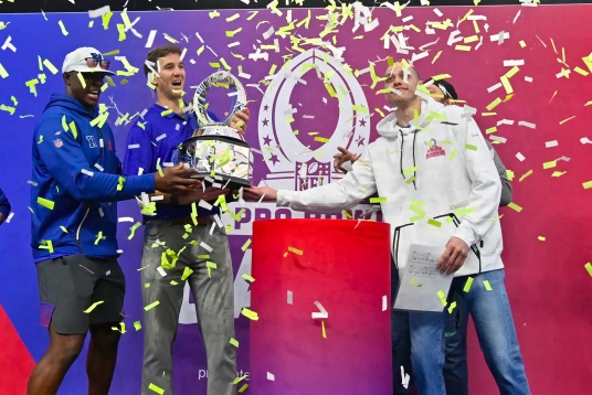 NFC head coach Eli Manning hoisting the pro bowl trophy, with assistant coach DeMarcus Ware (right) and NFC captain Pete Davidson (left).